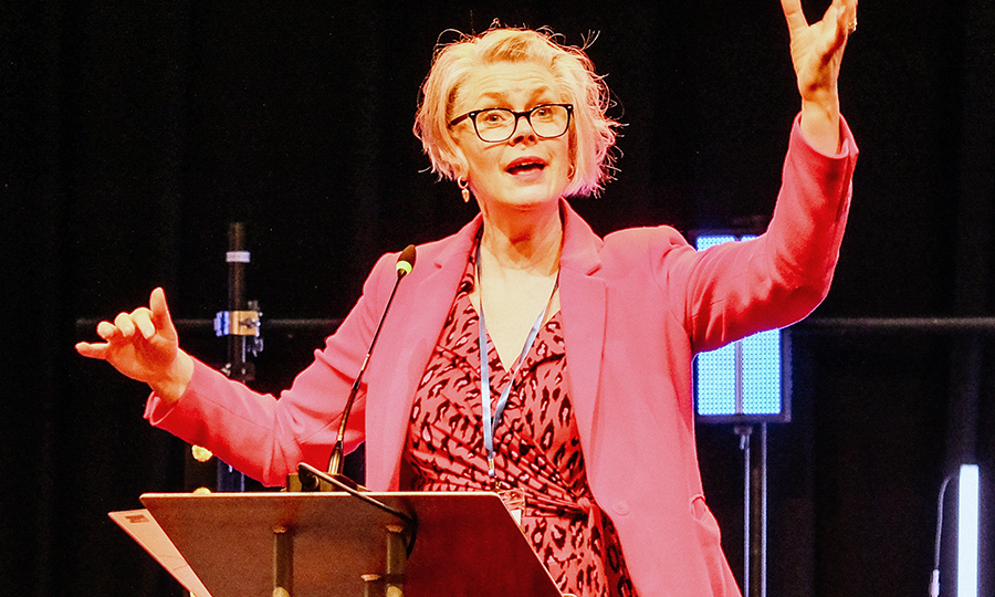 A woman in pink energetically conducting on a stage.