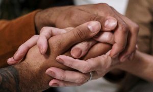 Two pairs of hands gently clasped, symbolising unity and support, warmth and solidarity.