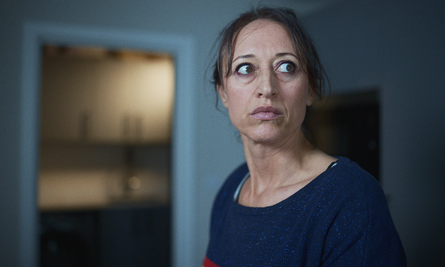A woman with a concerned expression looks to the side in a dimly lit room.