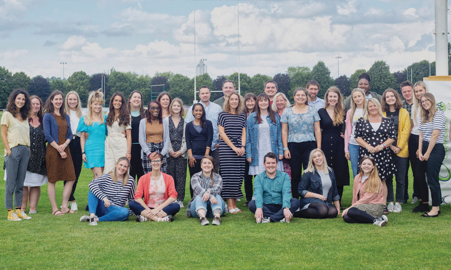 Harmless team smiling together on a grassy field with trees and a blue sky in the background.