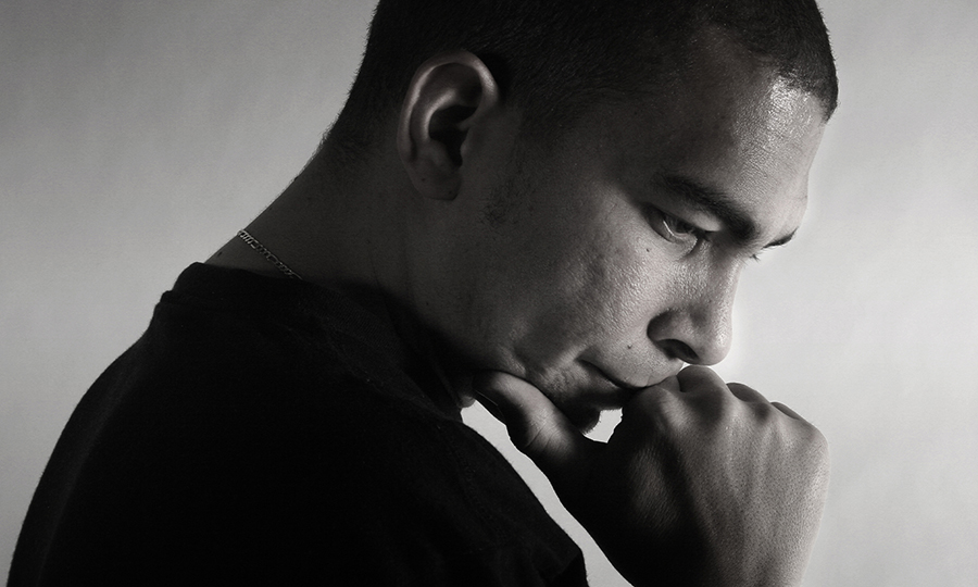 A man in profile with a shaved head rests his chin on his fist, gazing downwards in deep thought.