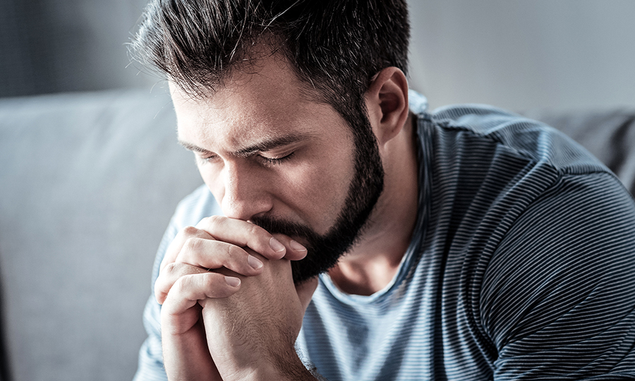 A man with a beard clasping his hands looking worried and contemplative.