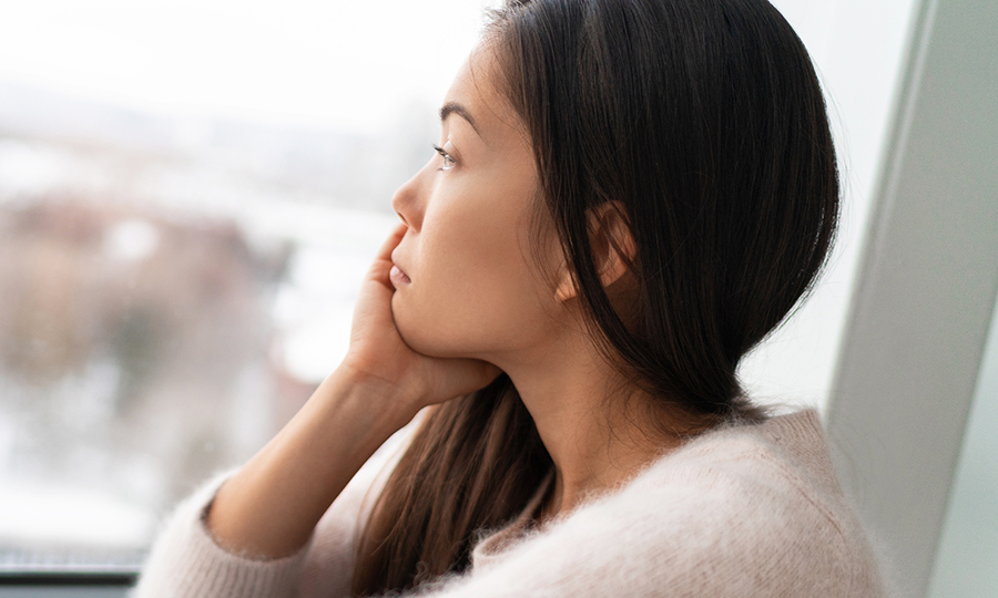 Woman gazes thoughtfully out a window, resting her chin on her hand.