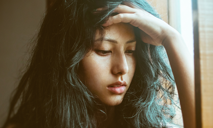A woman with long, dark hair deep in thought, rests her hand on her forehead.