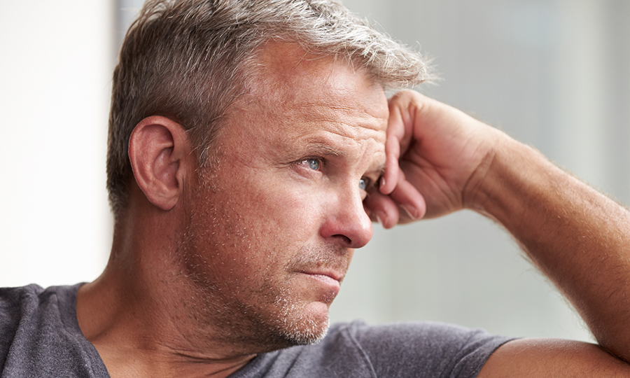 Man with short grey hair gazes thoughtfully out of the window, resting his head on his hand.