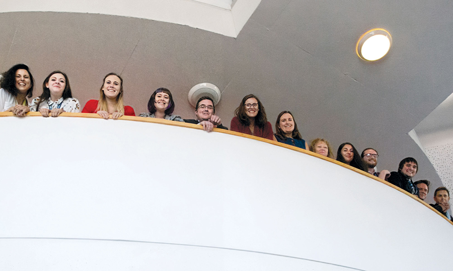 Members of the Harmless team stand smiling and leaning over a curved balcony.