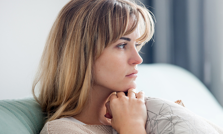 A woman with blonde hair looks thoughtfully out a window, resting her chin on her hands.